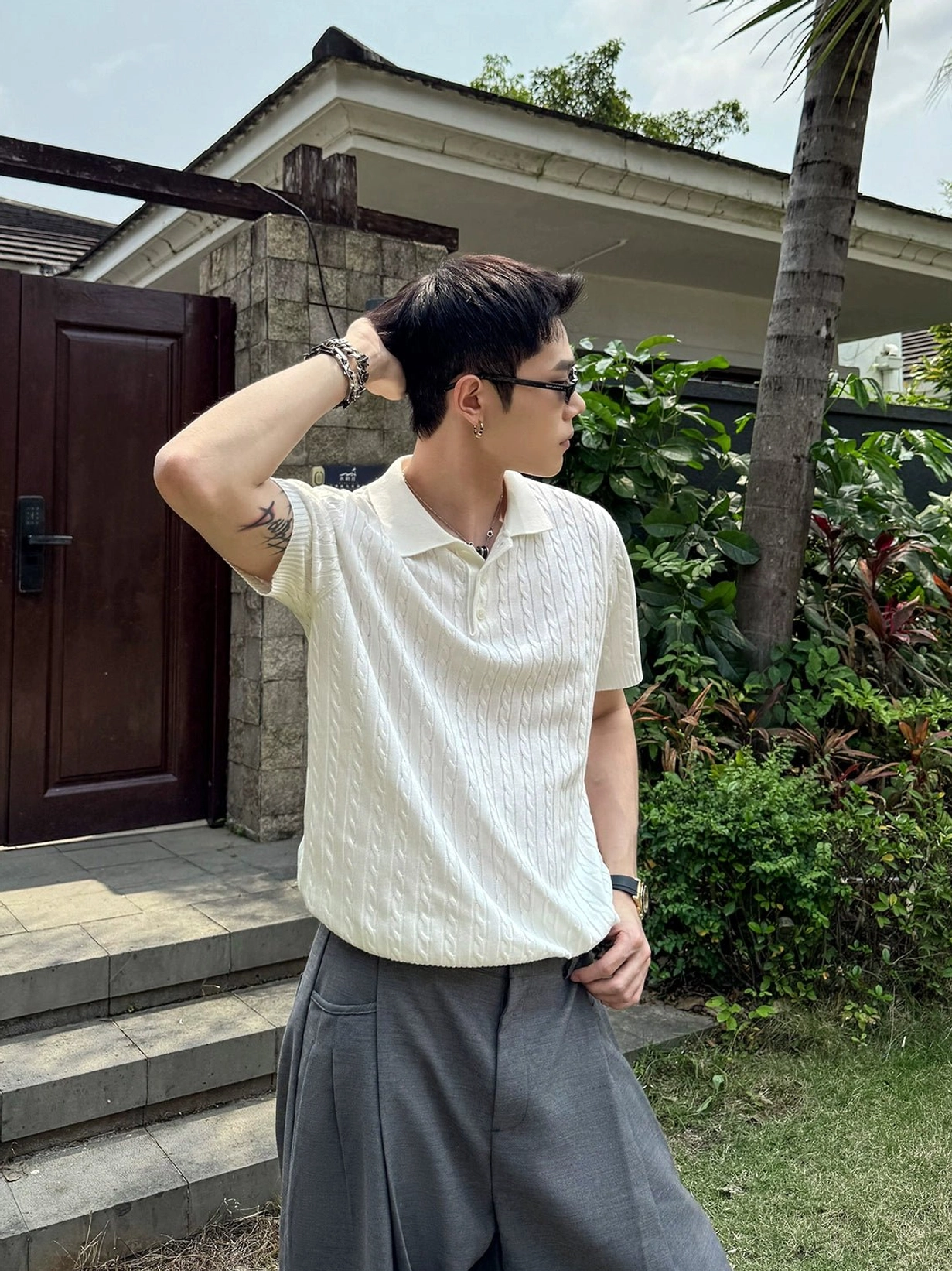 Cream cable knit short sleeve polo shirt with twisted textured pattern and relaxed silhouette photographed in a villa garden courtyard