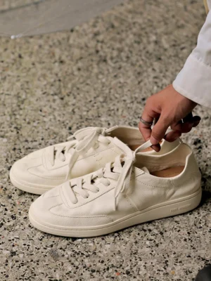 Cream cowhide leather low-profile sneakers viewed from above with long loose laces, tapered toe caps, and flat rubber soles