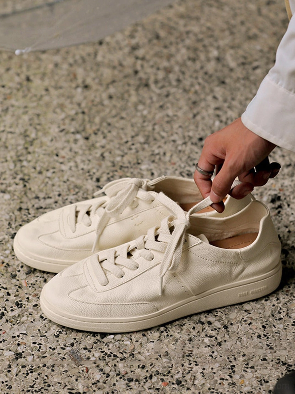 Cream cowhide leather low-profile sneakers viewed from above with long loose laces, tapered toe caps, and flat rubber soles