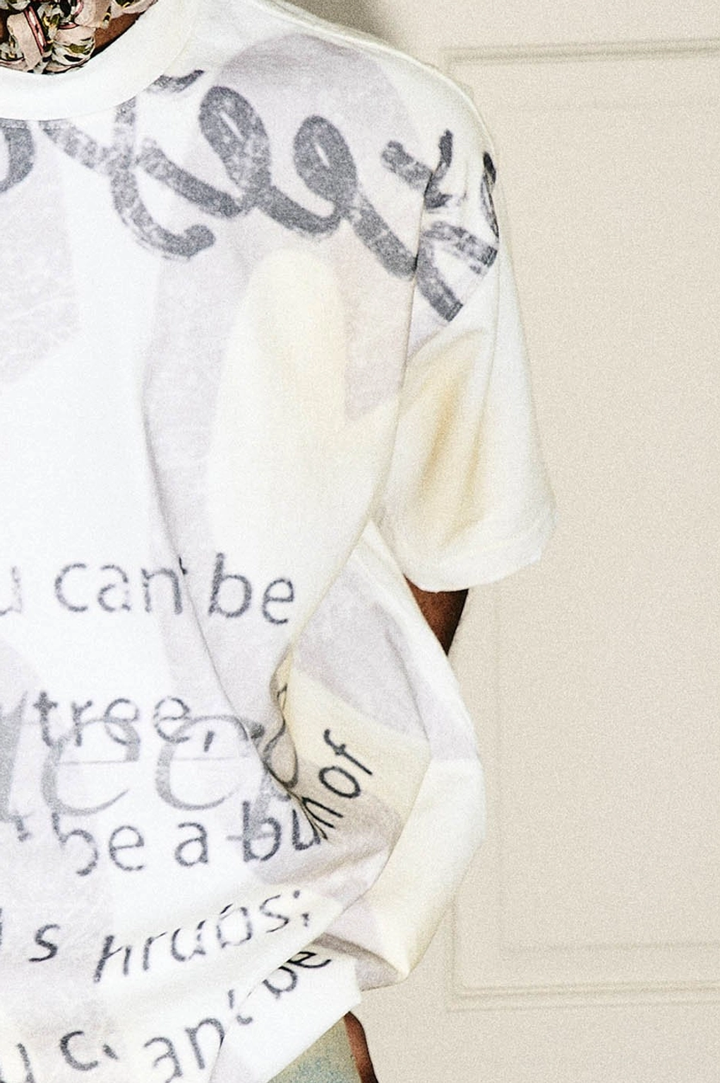 Side detail of a cream faded oversized graphic T-shirt showing the relaxed silhouette and gray printed lettering