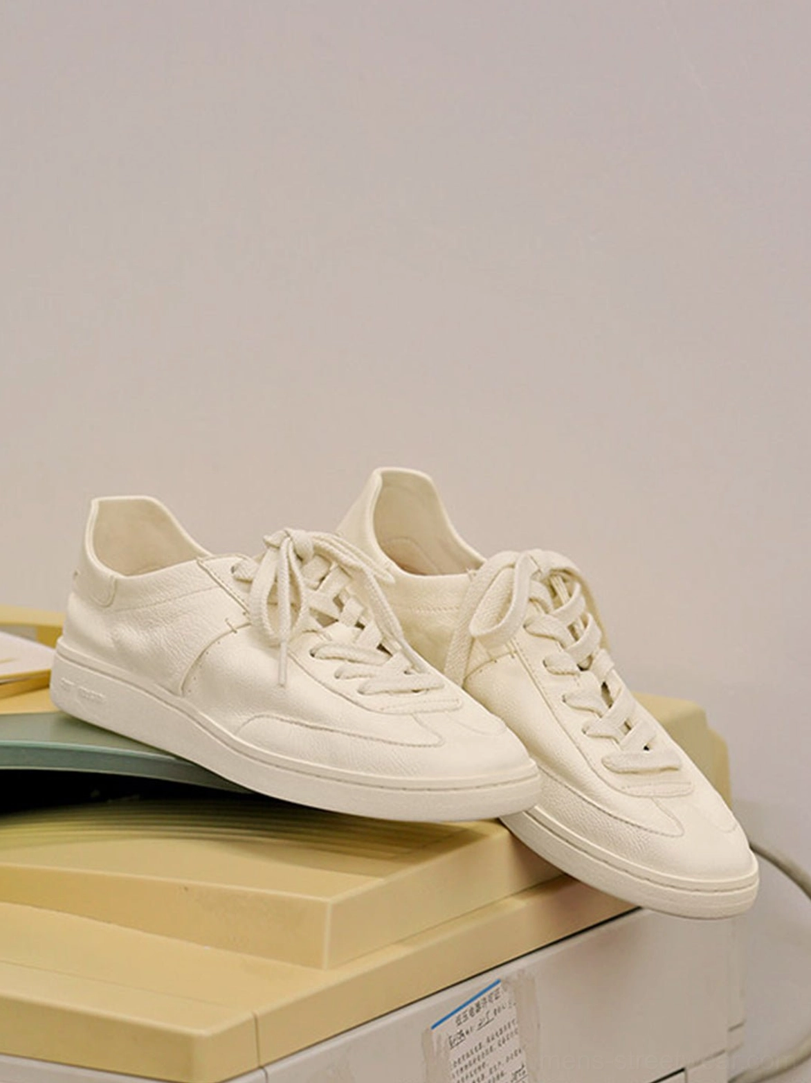 Cream low-profile cowhide leather sneakers displayed on stacked storage boxes with subtle side panels and a clean minimalist finish