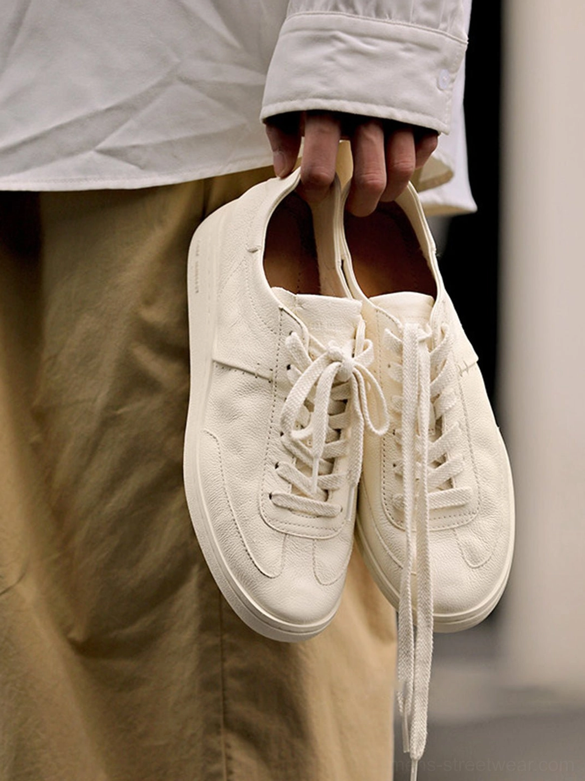 Close-up of cream low-top cowhide leather sneakers with neat stitching, classic laces, and a smooth soft leather upper