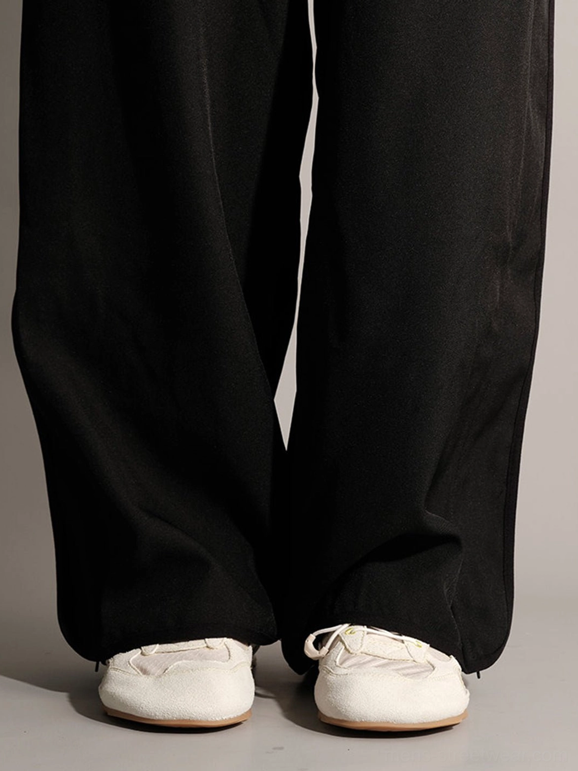 Model wearing cream nubuck low-profile sneakers with black wide-leg trousers in a minimalist streetwear outfit
