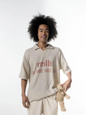 Model wearing an oversized cream waffle knit polo shirt with vintage red chest graphic and beige wide-leg trousers in a minimalist studio