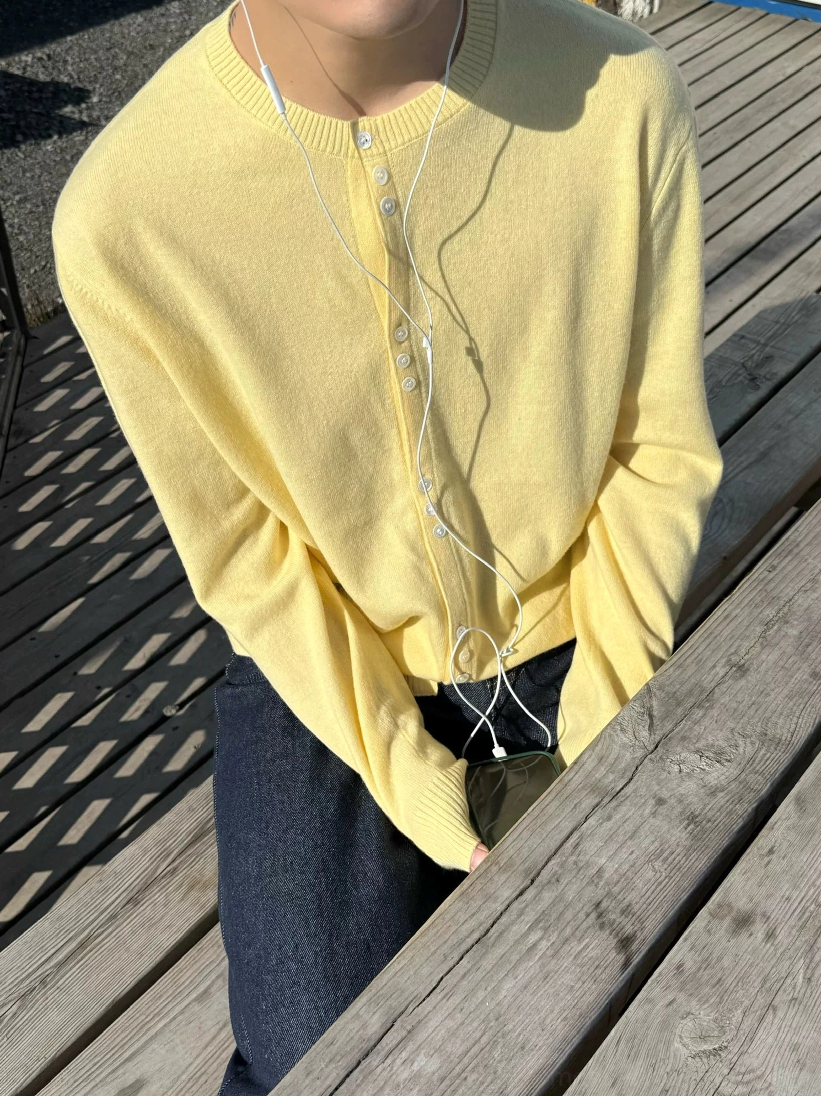 Close-up view of creamy yellow lambswool henley knit cardigan showing soft texture and button neckline with dark wide-leg jeans