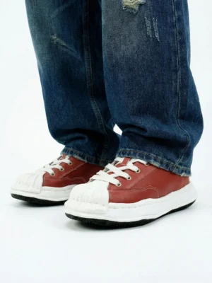 Crimson red shell-toe streetwear sneakers styled with blue ripped straight-leg jeans in a low front view