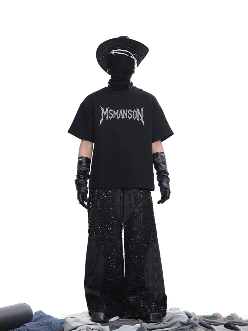 Full body back view of cropped boxy black gothic script T-shirt styled with glitter wide-leg pants and avant-garde streetwear accessories