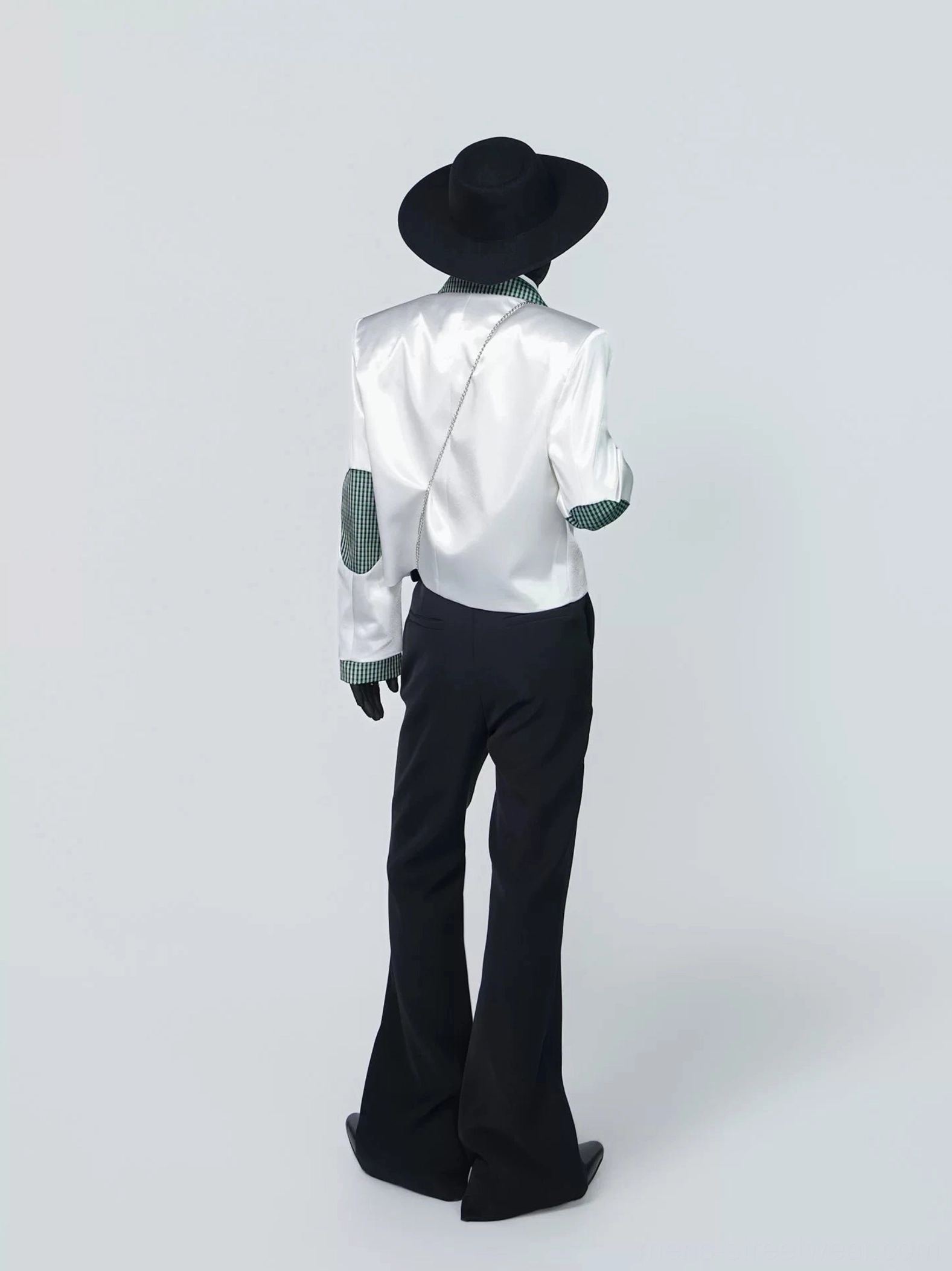 Back view of a cropped white tuxedo blazer showing green houndstooth elbow patches and a chain strap detail