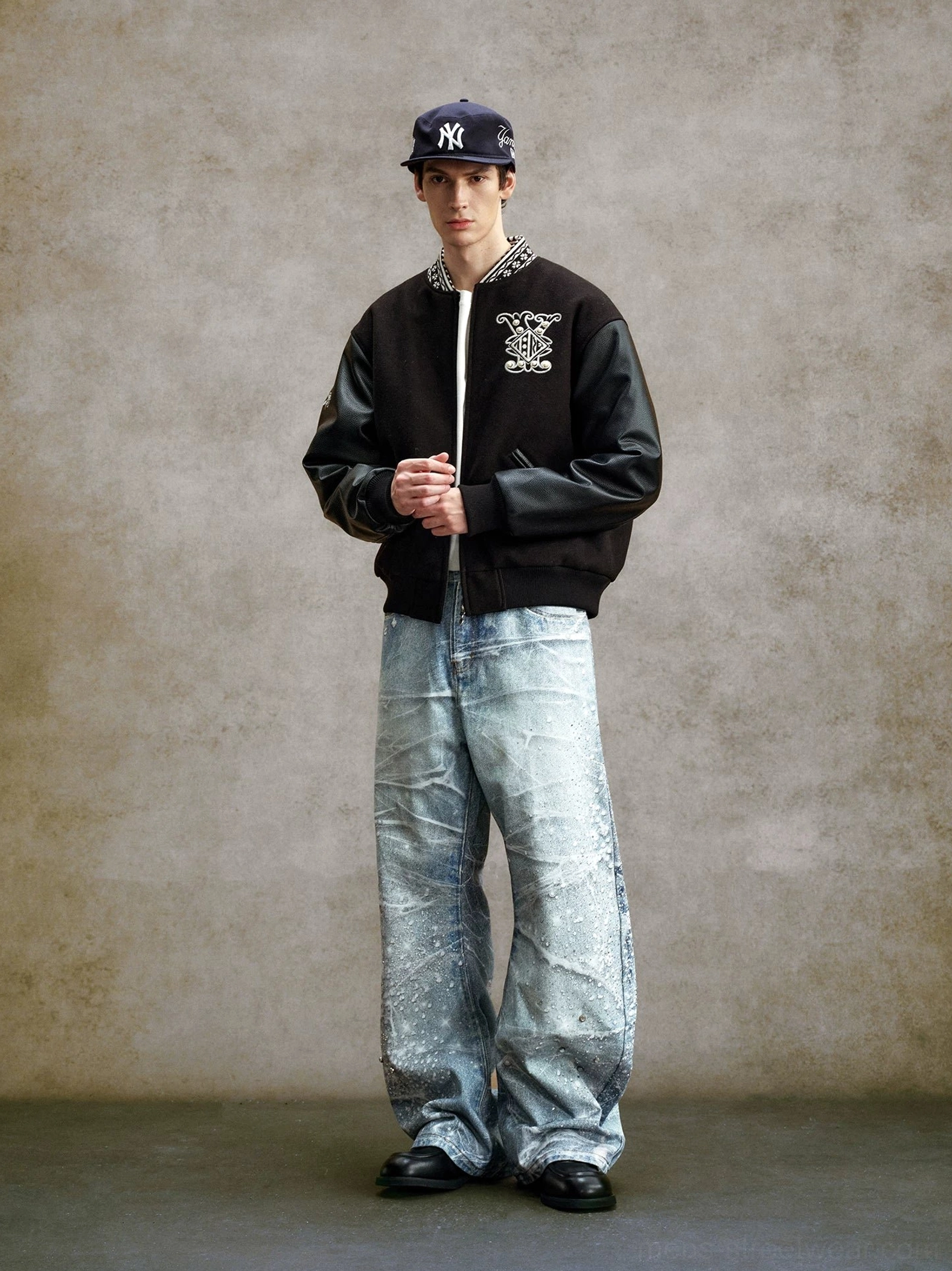 Full body styling view of crystal embellished acid wash wide leg jeans worn with a varsity jacket, baseball cap, and black leather loafers in Korean streetwear style