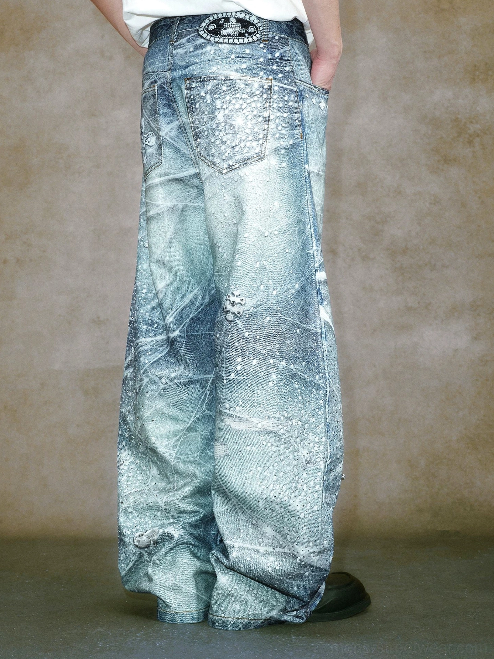 Rear view of crystal embellished acid wash wide leg jeans showing scattered rhinestones, distressed light blue denim, rear patch detail, and oversized stacked streetwear fit