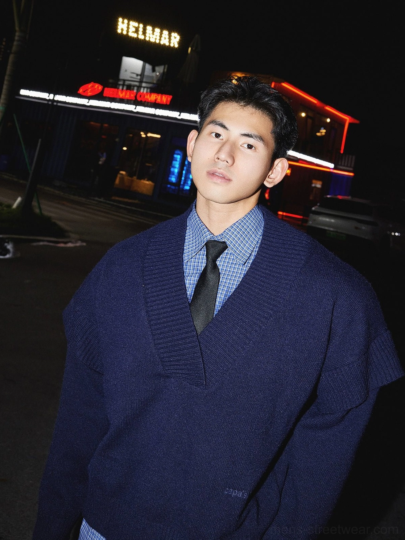 Dark blue deep V-neck knit sweater layered with blue checked shirt and black tie in a Korean campus streetwear look