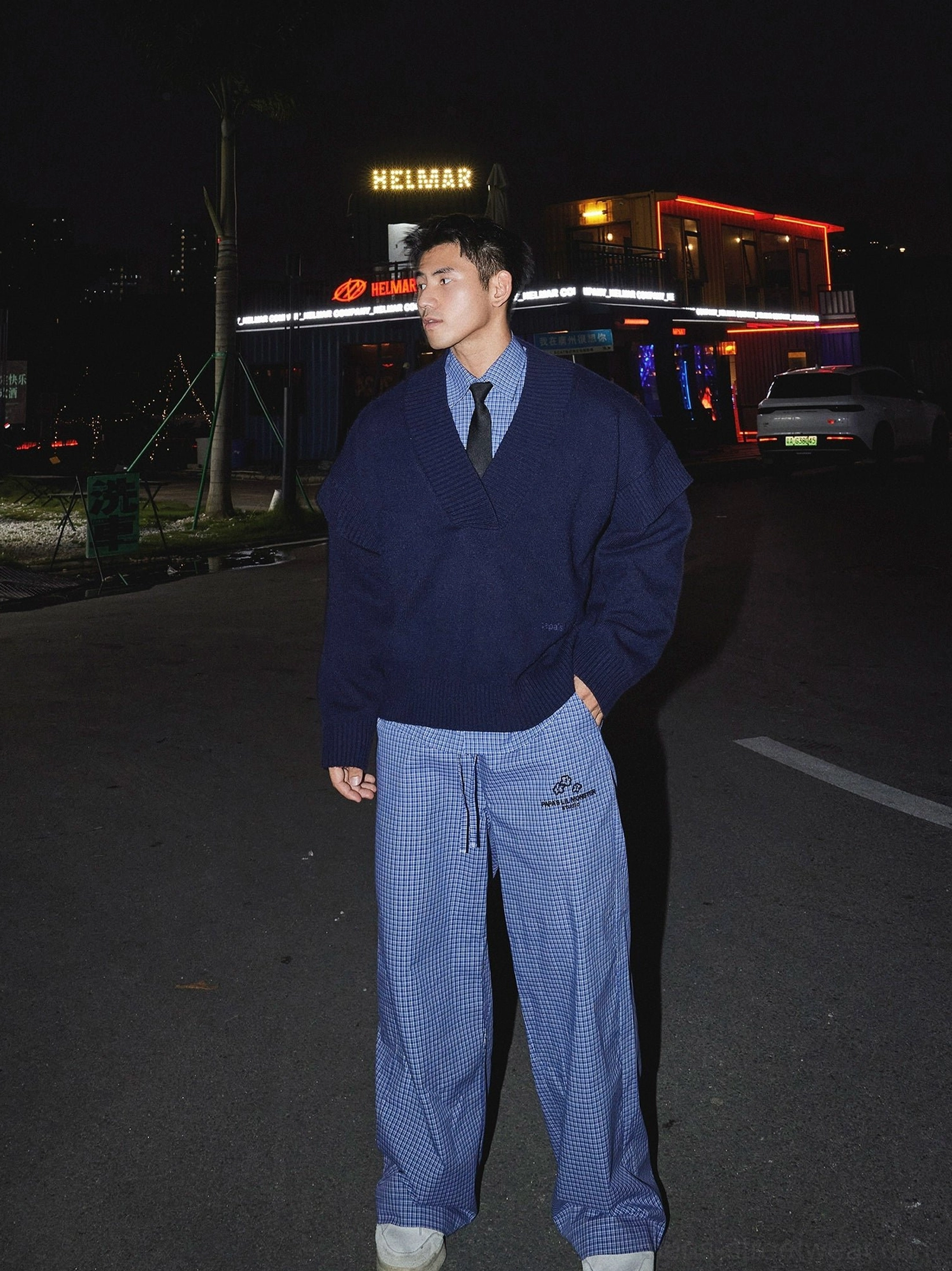Dark blue oversized deep V-neck knit sweater with checked shirt and loose plaid trousers on a nighttime city street