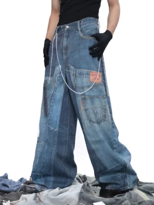 Low angle front view of dark blue patchwork wide-leg jeans with faded denim panels, distressed texture, utility pockets, leather waist patch, and detachable bead chain