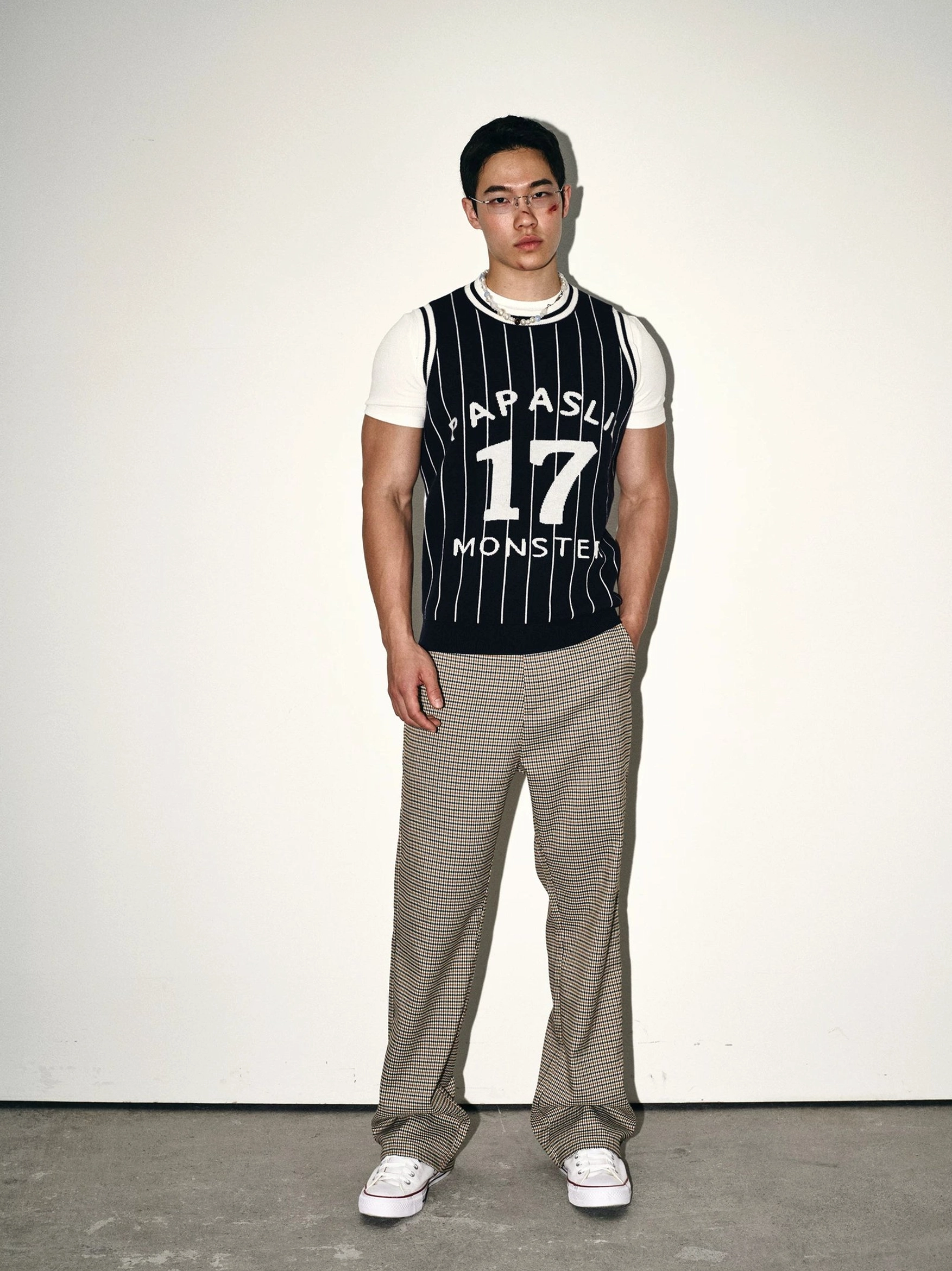 Dark blue pinstripe varsity knit basketball jersey vest layered over a white t-shirt with checkered trousers in a full-body streetwear outfit