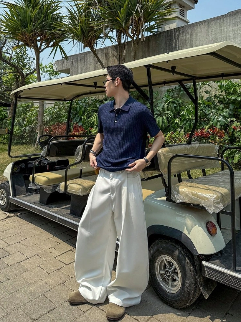 Dark blue short sleeve textured knit polo shirt styled with white wide leg trousers beside a resort golf cart