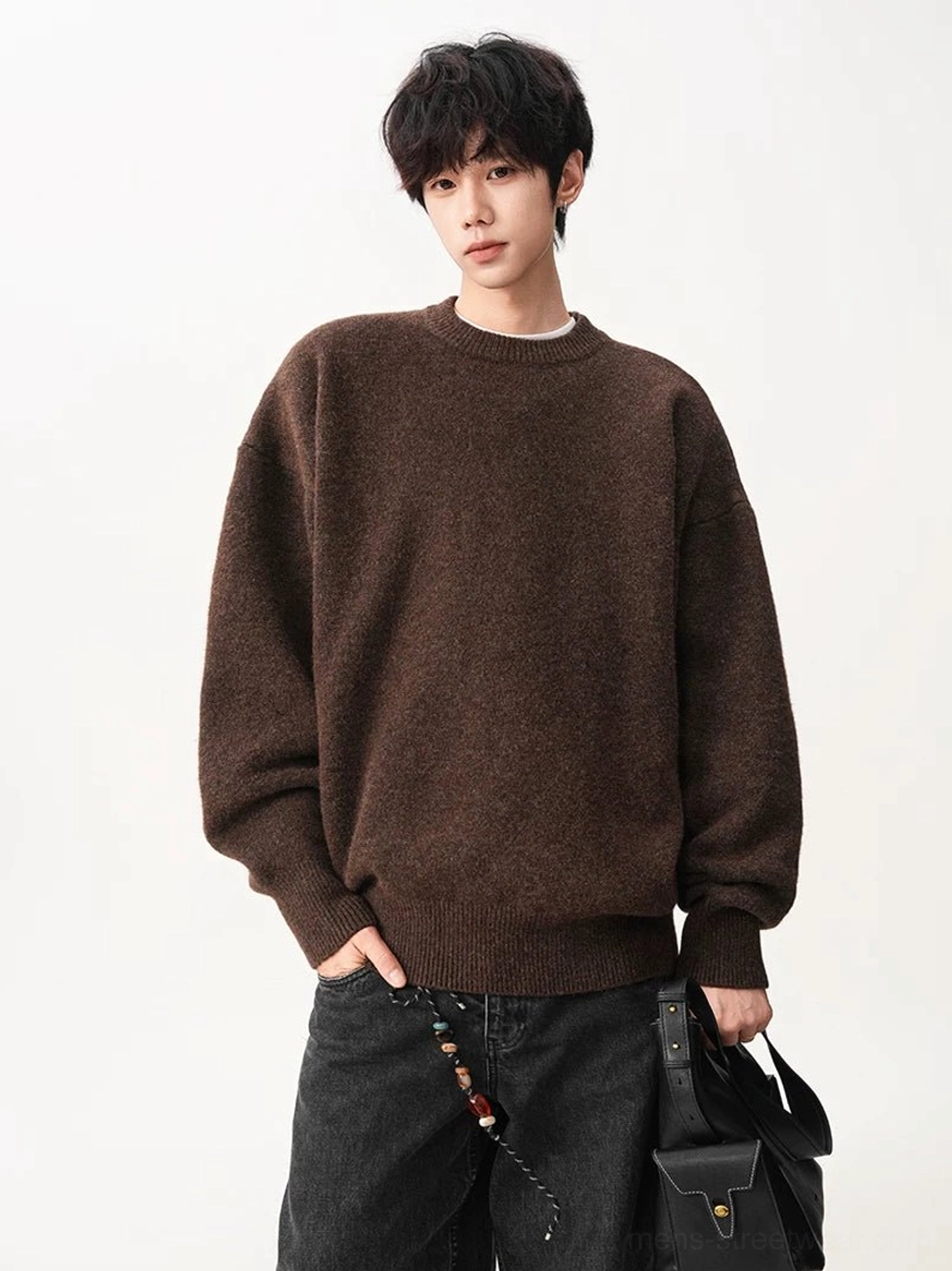 Male model wearing a dark brown fuzzy oversized crew neck sweater with relaxed sleeves and ribbed trims alongside a black leather bag