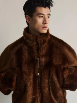 Close-up front view of dark brown high-pile faux fur bomber jacket showing plush texture stand collar zipper and raglan sleeves