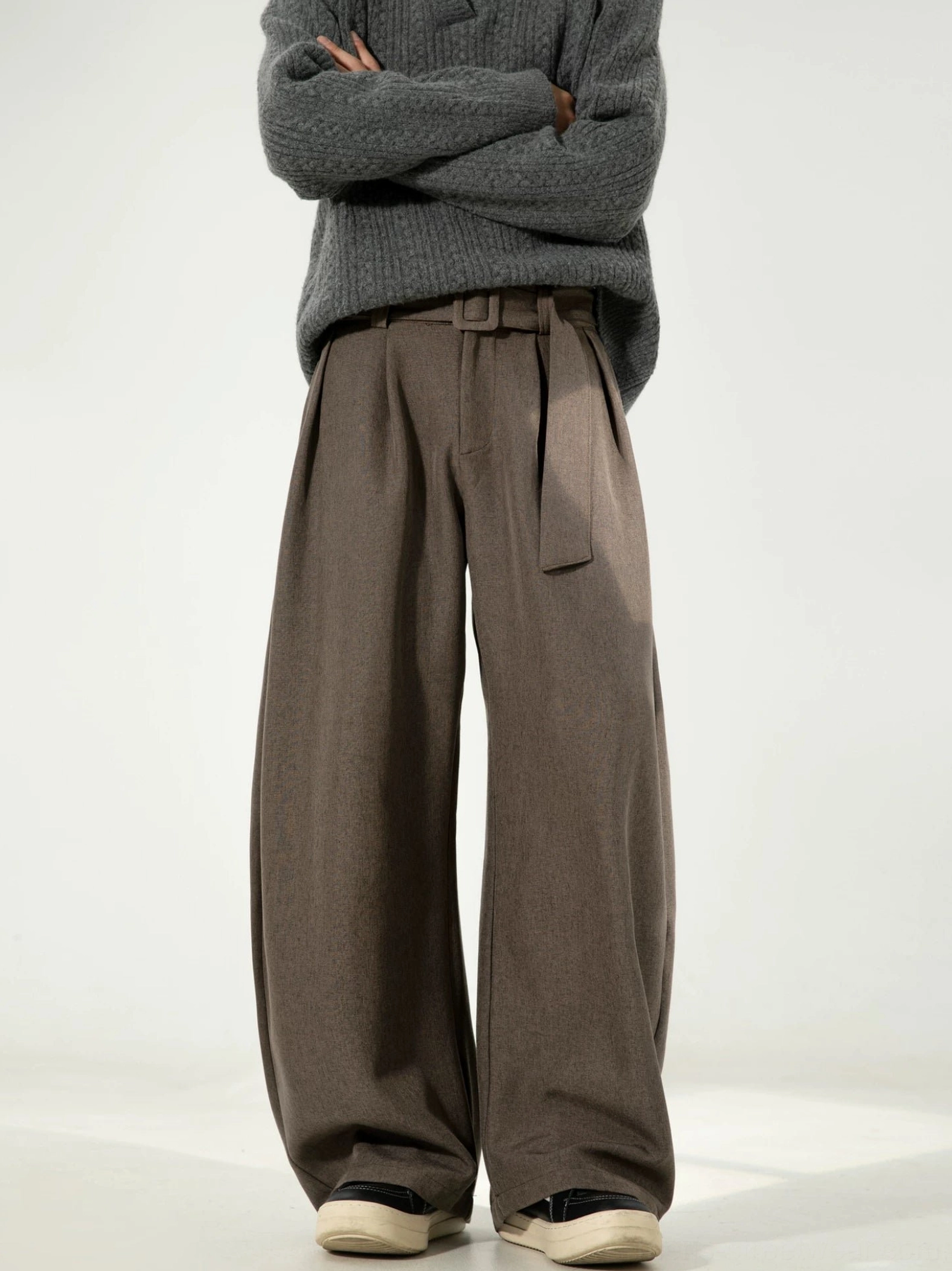 Male model wearing dark brown linen-texture curve trousers with front pleats, relaxed wide legs, and a matching waist belt