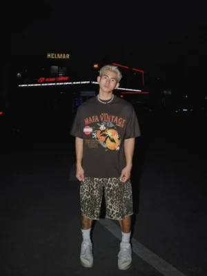 Dark brown oversized citrus graphic T-shirt with distressed retro print styled with patterned shorts in nighttime streetwear scene