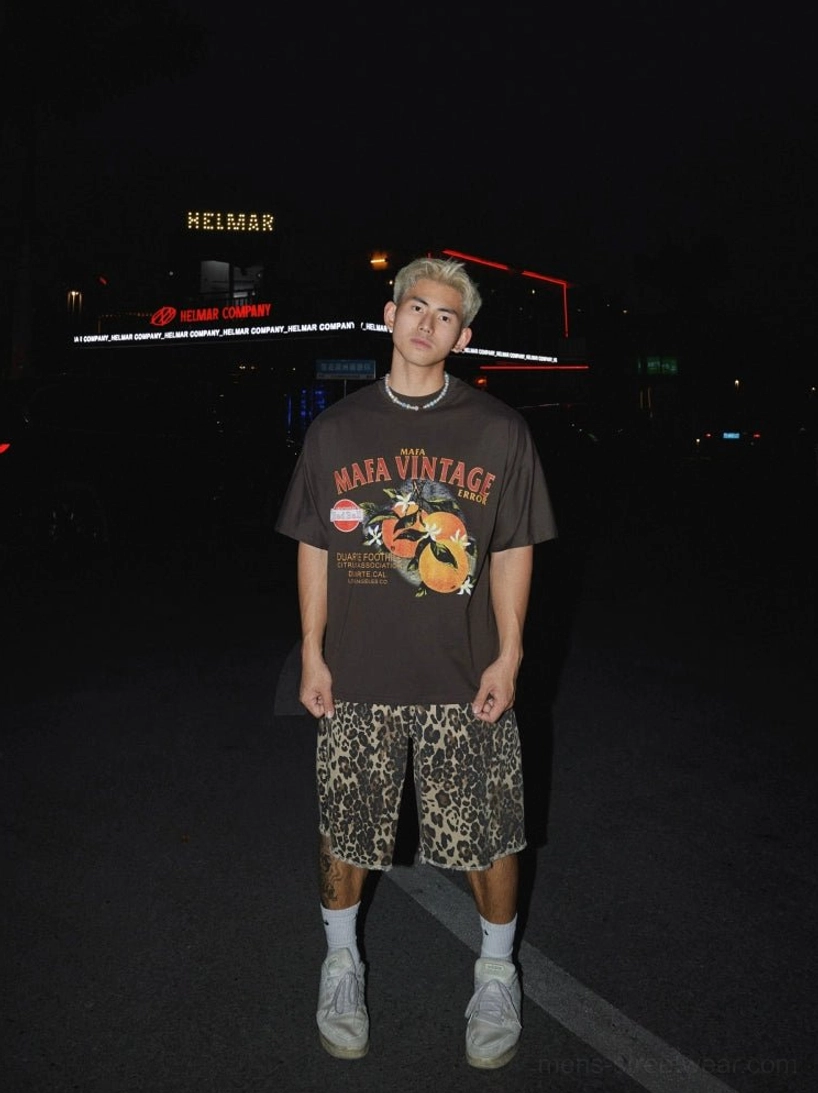 Dark brown oversized citrus graphic T-shirt with distressed retro print styled with patterned shorts in nighttime streetwear scene