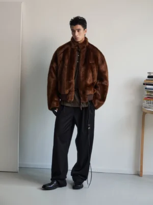 Dark brown oversized faux fur bomber jacket worn by male model in a minimalist studio front view with stand collar and ribbed hem