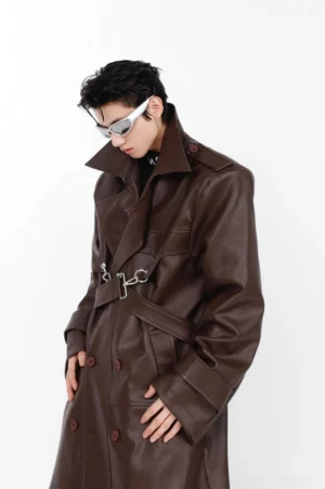 Dark brown oversized vegan leather trench coat shown from a three quarter view with matte PU finish double breasted buttons shoulder epaulets metal chest buckle and longline streetwear silhouette