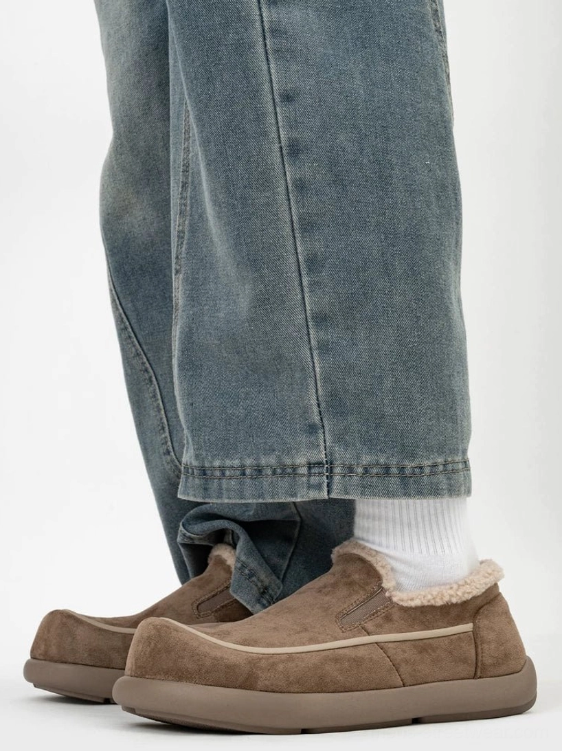 Dark brown shearling-lined slip-on clogs worn with white socks and baggy jeans, showing the contrast stitching, fleece collar, and flat rubber sole