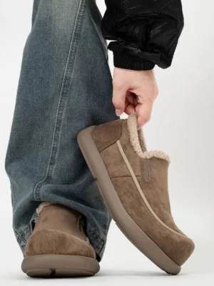 Dark brown shearling-lined slip-on winter clogs worn with baggy jeans, showing the fuzzy collar, suede-finish upper, contrast stitching, and thick rubber streetwear sole