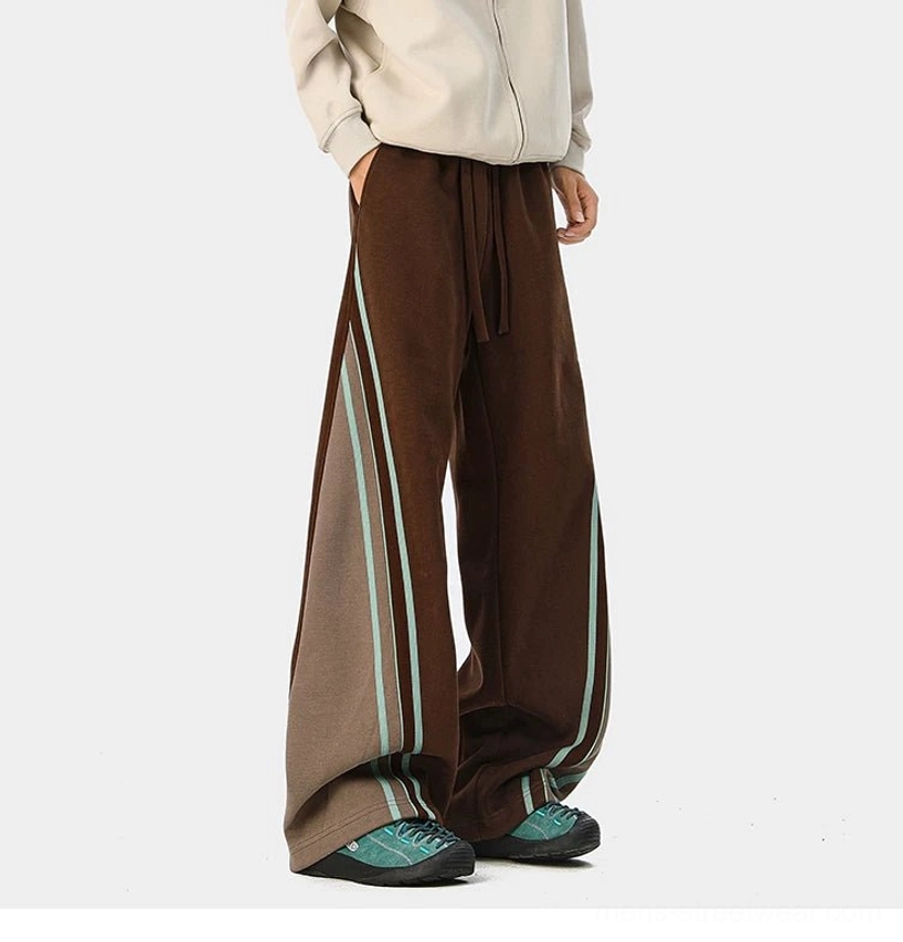 Three-quarter view of dark brown wide-leg varsity track pants with light brown side patch, cyan stripes, and drawstring waist