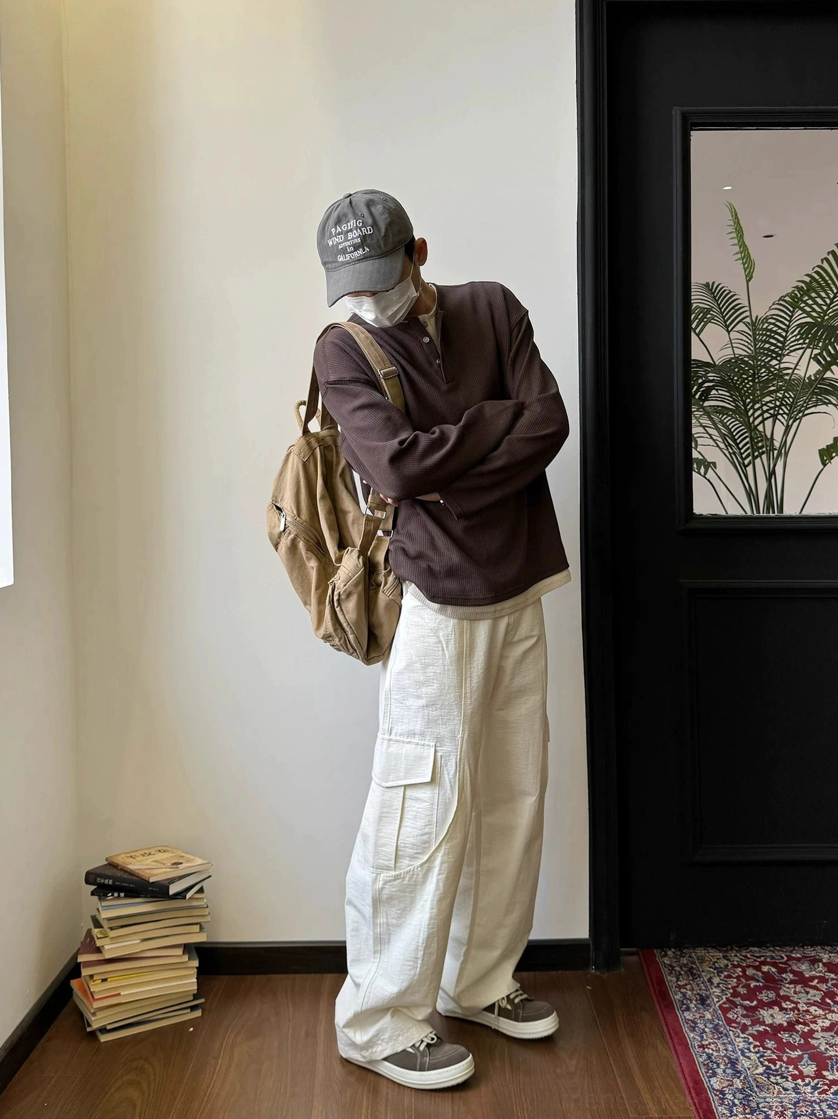 Male model wearing a dark brown waffle knit Henley shirt with cargo pants, sneakers and a canvas backpack