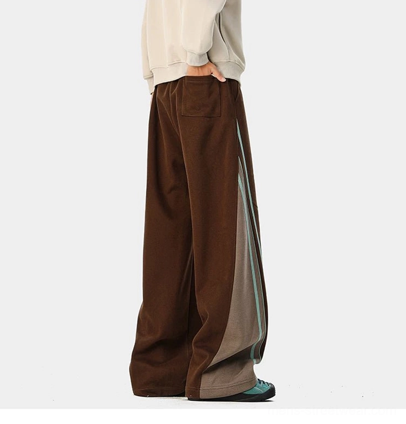 Back view of dark brown wide-leg varsity track pants with side color block, light cyan stripes, rear waist pocket, and loose fit