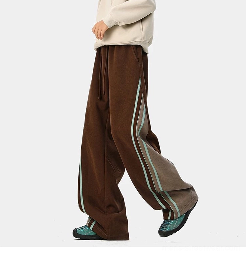 Side view of relaxed dark brown wide-leg varsity track pants with matching stripe trims and oversized streetwear silhouette
