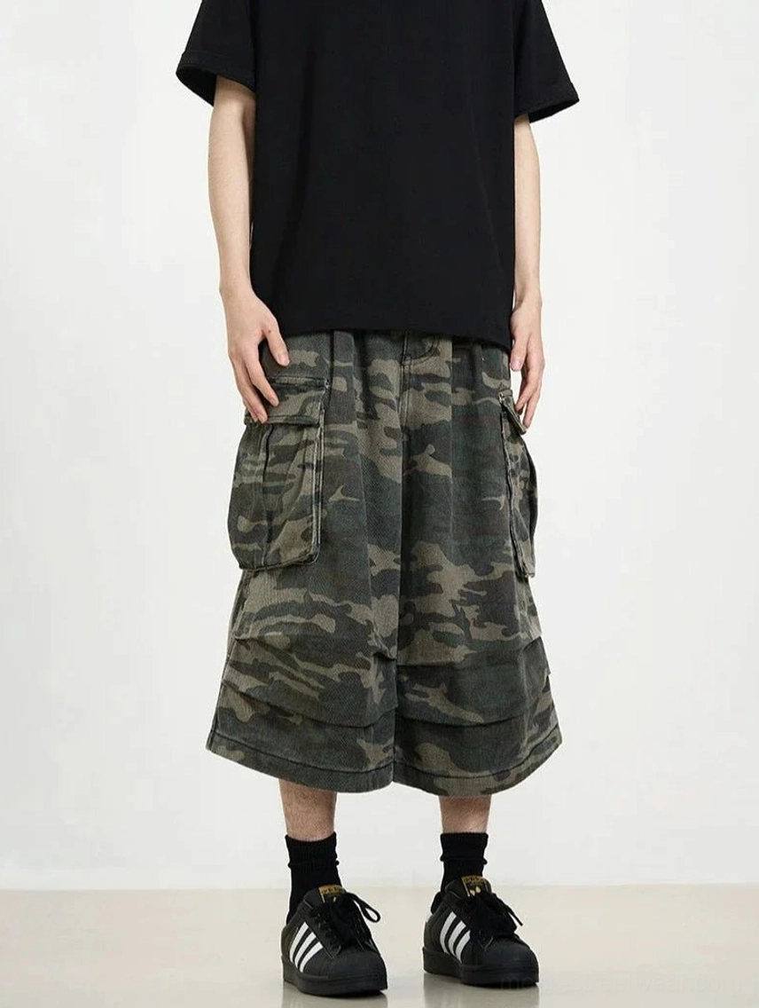 Front view of dark camouflage cropped cargo shorts showing the oversized silhouette, layered hem, and large side pockets