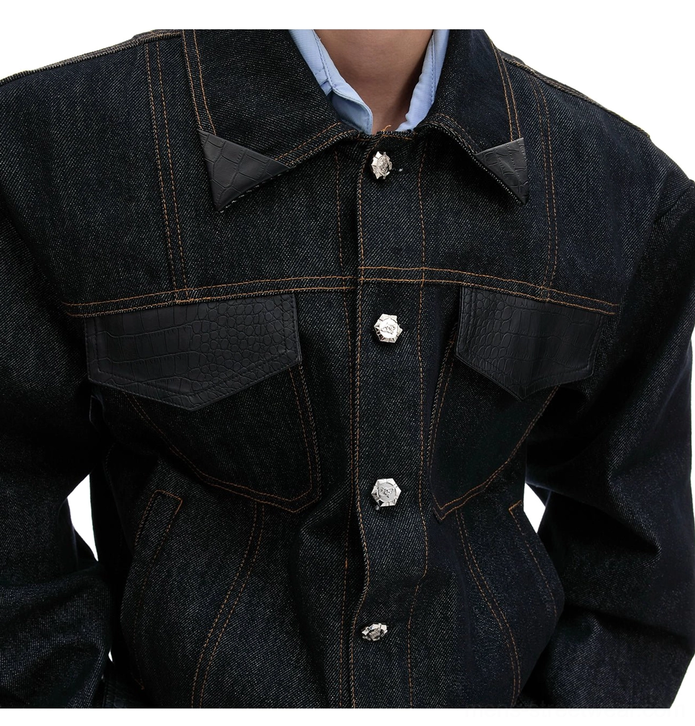 Close-up view of an oversized dark denim jacket showing leather-trimmed collar, crocodile-textured chest pocket panels, contrast stitching, and decorative metal floral buttons
