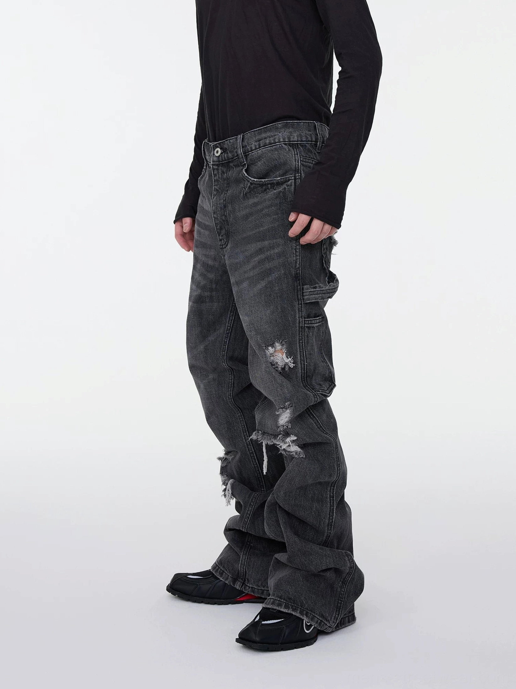 Side view detail of washed black gray distressed stacked denim jeans with cargo utility pocket strap and flared leg