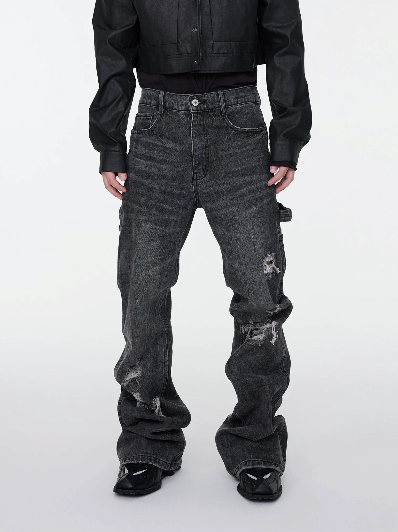 Male model wearing dark gray distressed stacked flare cargo denim jeans with ripped details and utility pocket front view