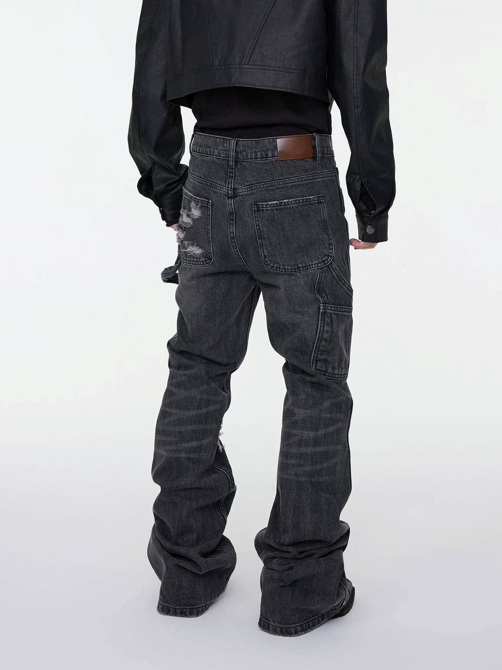 Rear view of dark gray stacked flare denim jeans showing back patch pockets leather patch and extended stacked hem