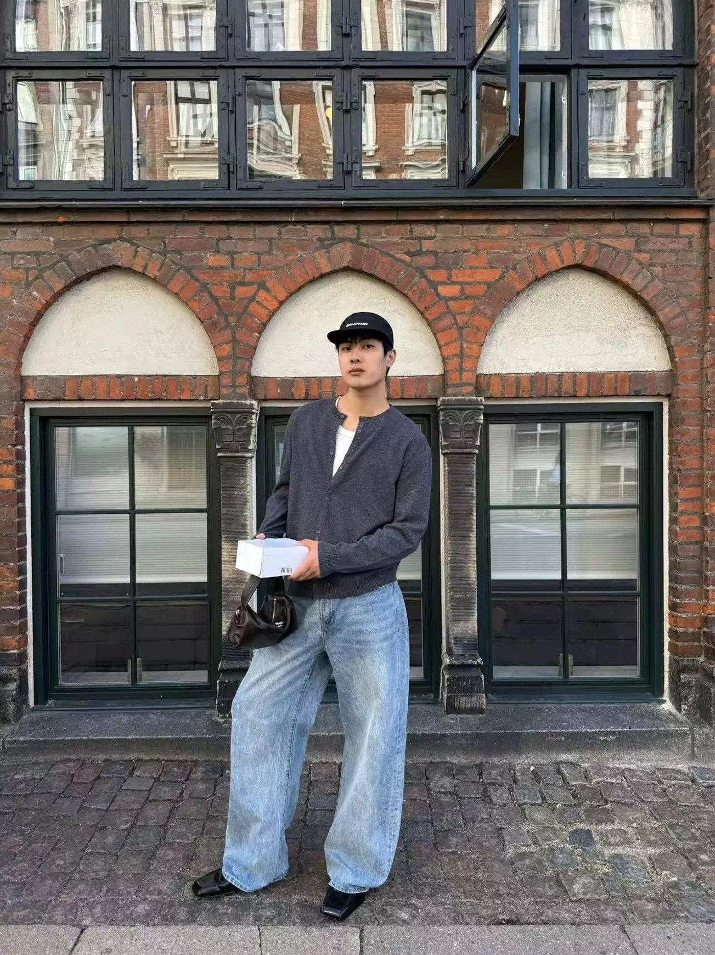 Dark gray henley knit cardigan full front view with minimalist button neckline on a male model near a brick arched window