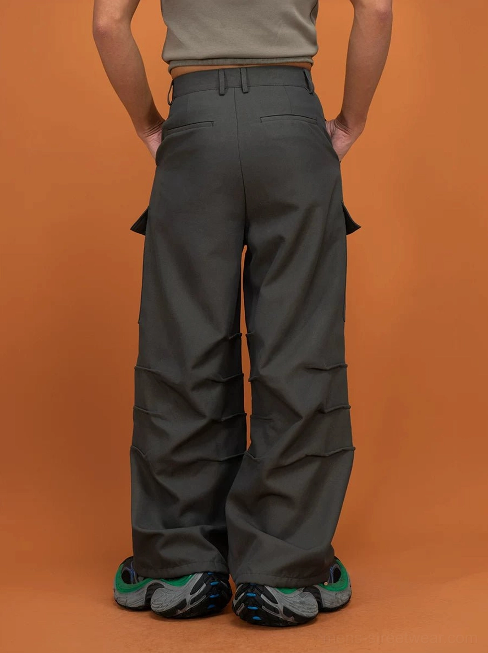 Dark gray layered cargo pants shown from the full rear view with back pockets, oversized thigh pockets, and wide straight legs