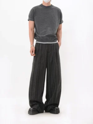 Dark gray textured knit mock neck T-shirt with rolled short sleeves and visible layered white hem worn with pleated striped wide leg trousers