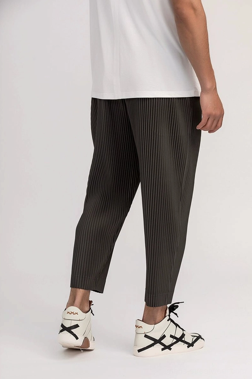 Back view of dark gray men's pleated cropped pants showing drapey relaxed fit, even texture, elastic waist, and ankle-length hem