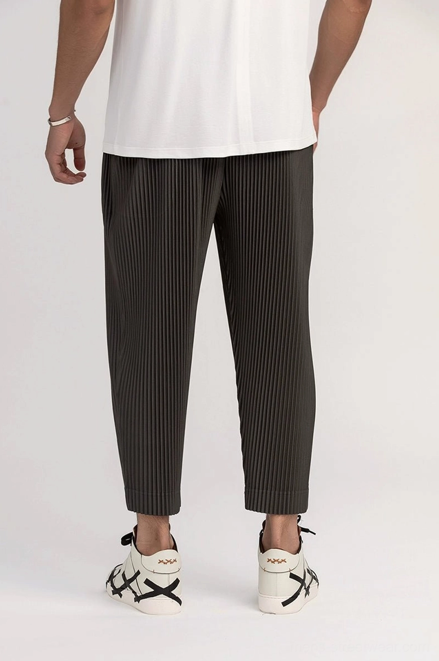 Dark gray relaxed pleated cropped trousers for men shown from a side front angle with white T-shirt and casual lace-up sneakers
