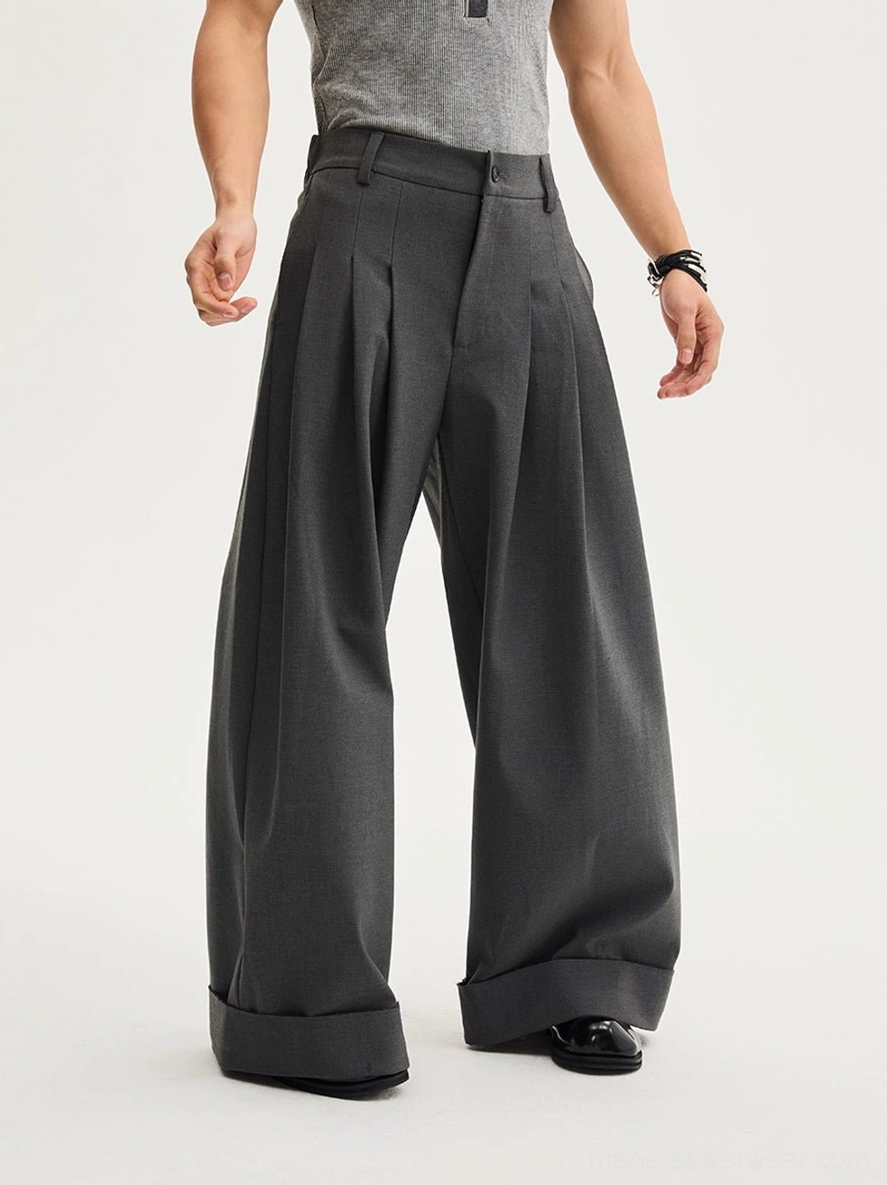 Dark gray oversized pleated wide-leg trousers with rolled cuffs styled with leather dress shoes in a minimalist modern menswear studio