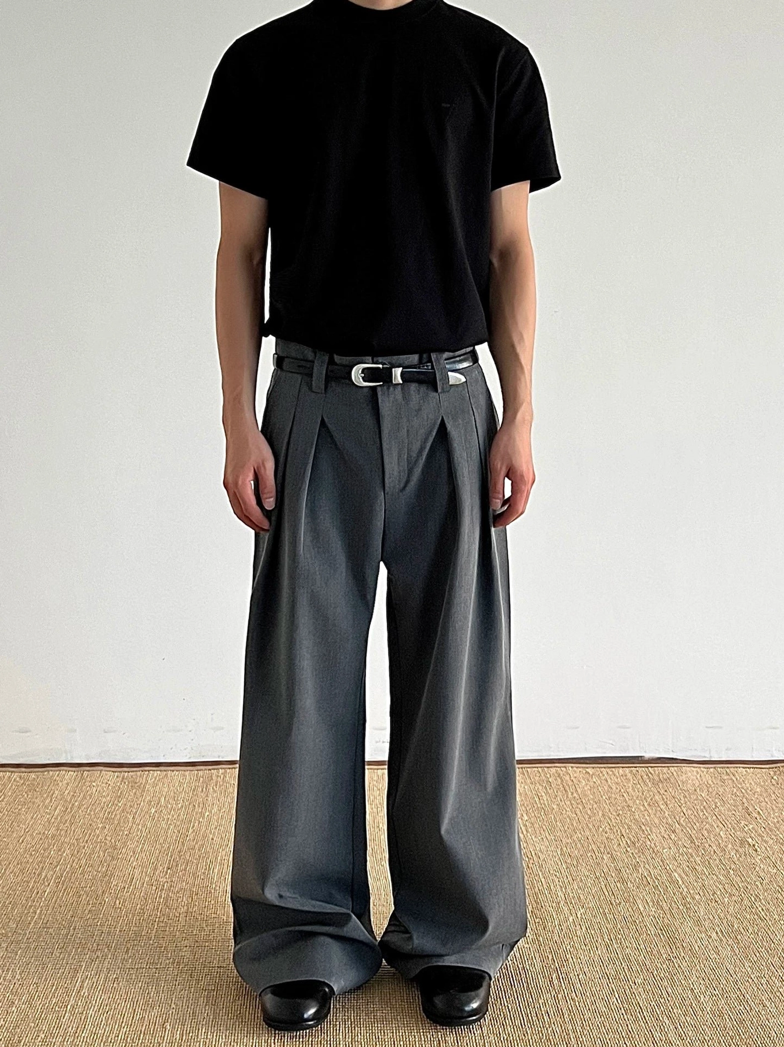 Dark gray pleated wide-leg tailored trousers worn with a black t-shirt and leather shoes in a minimalist Seoul streetwear outfit front view