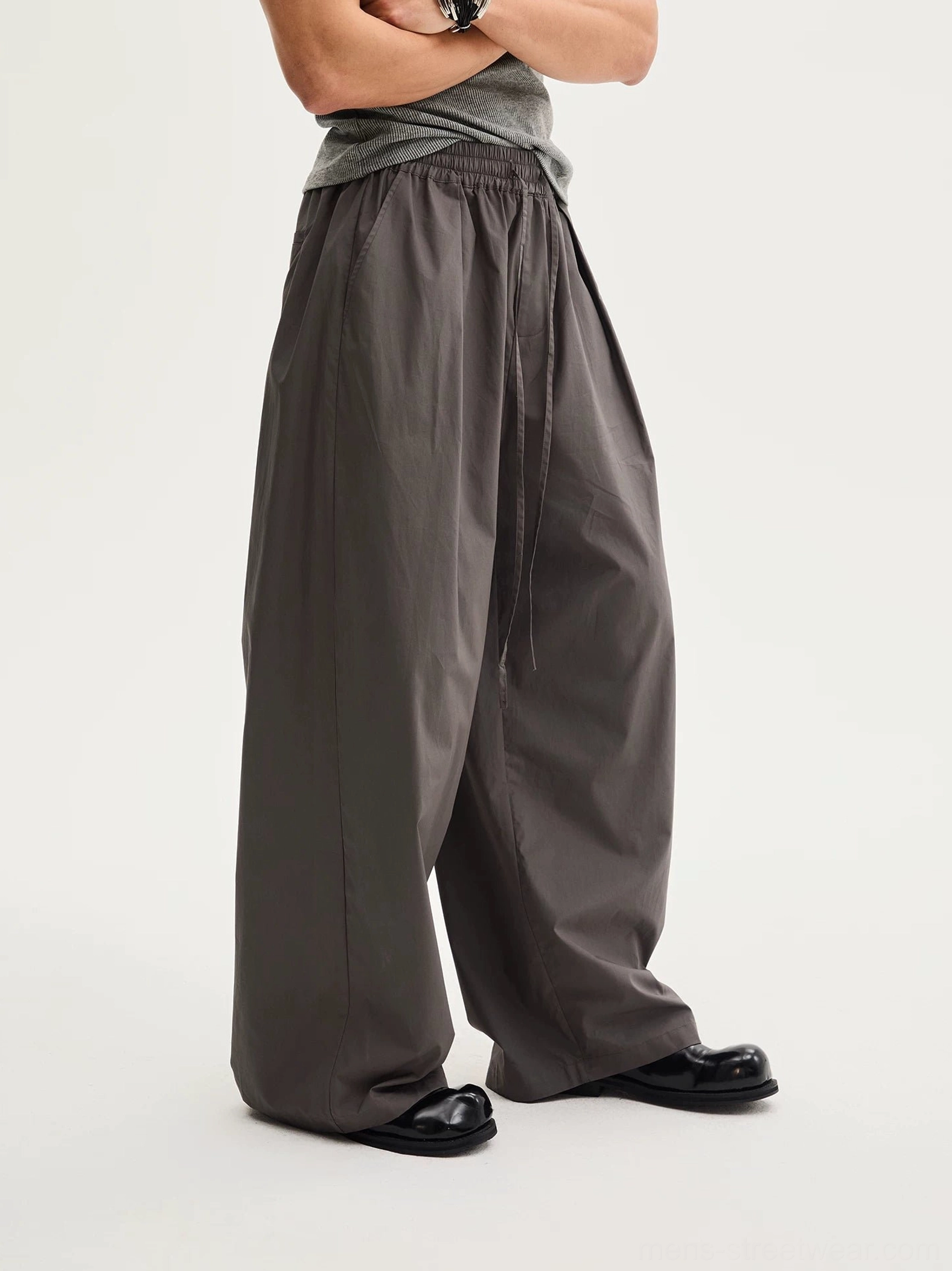 Dark gray relaxed wide-leg cotton pants shown in a low-angle close-up with elastic drawstring waist, front pleats, curved leg shape, and fluid full-length drape