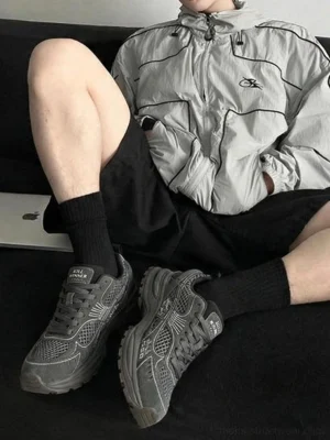 Dark gray retro running sneakers styled with a casual streetwear outfit, windbreaker, shorts, and relaxed urban look