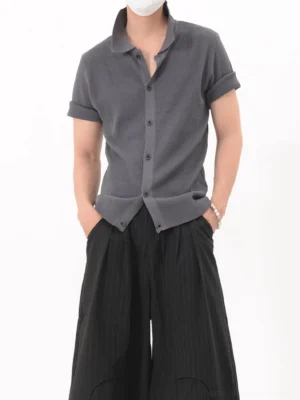 Dark gray textured knit polo shirt with button front, rolled short sleeves, curved hem, and wide-leg streetwear trousers