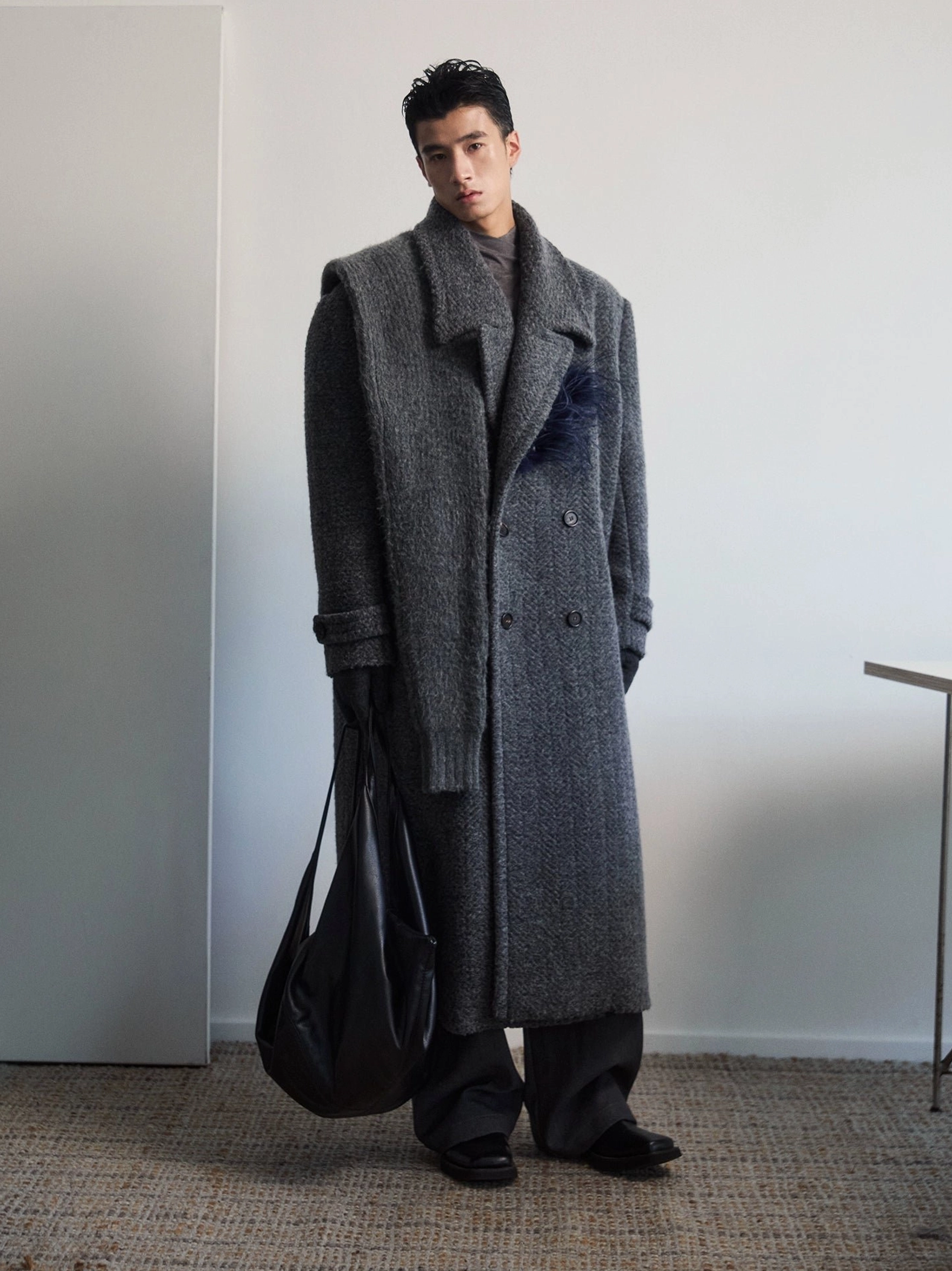 Men's dark gray textured wool double-breasted overcoat with detachable feather-inspired lapel brooch and black leather tote bag