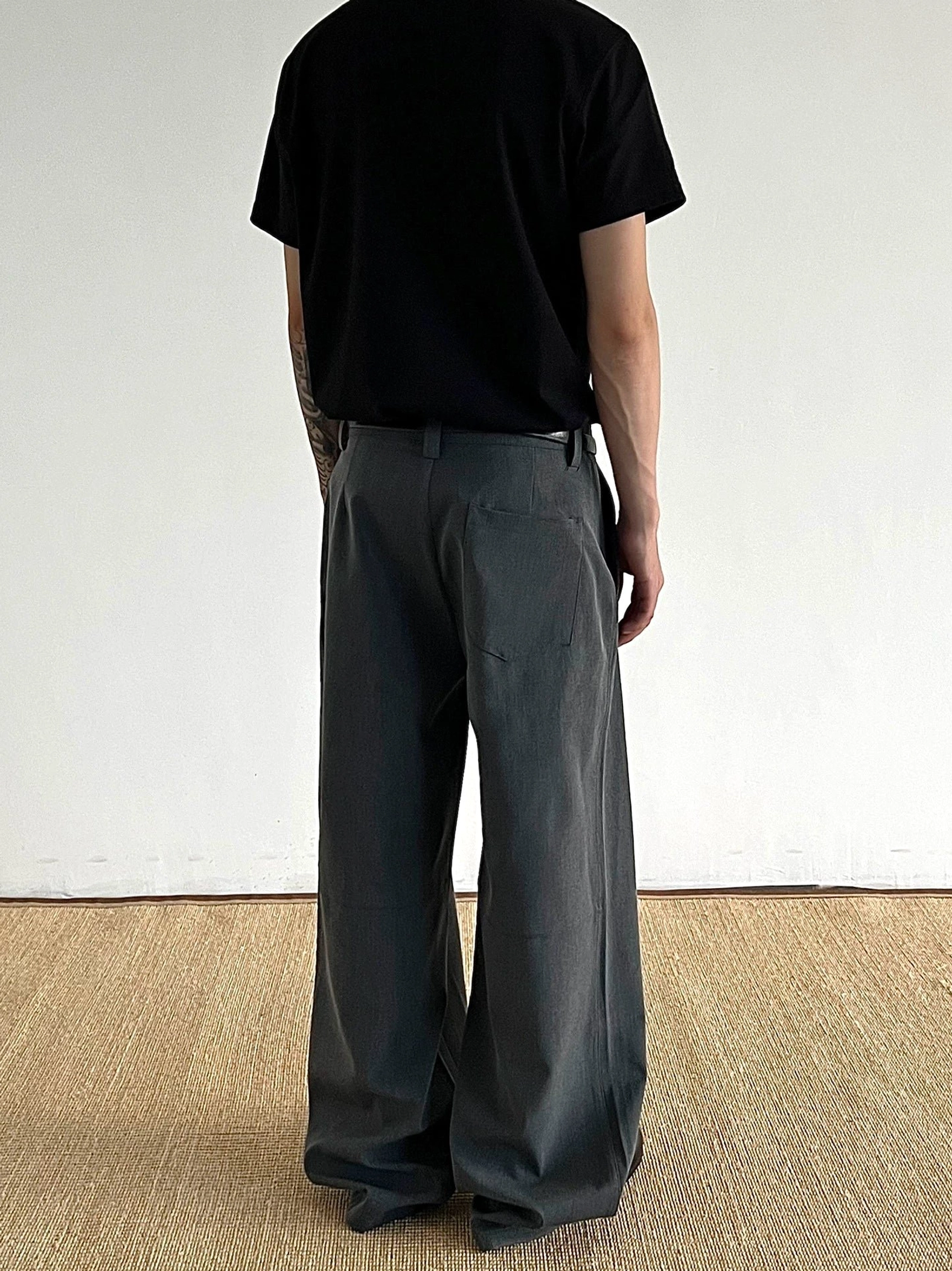 Back view of dark gray wide-leg pleated trousers showing structured waistband and rear patch pocket details