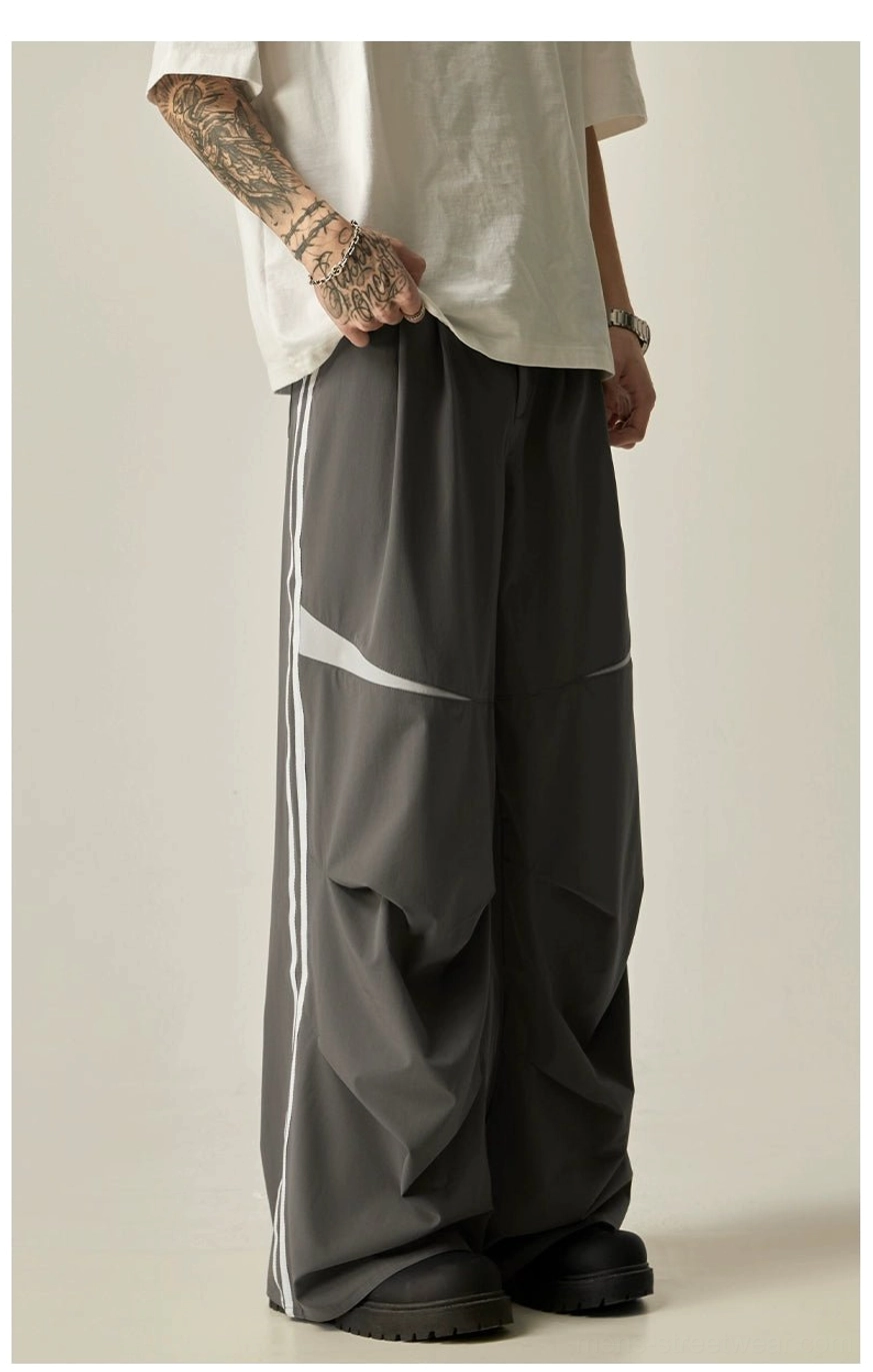 Back three-quarter view of dark gray wide-leg track pants with side stripes, rear patch pockets, and oversized fit